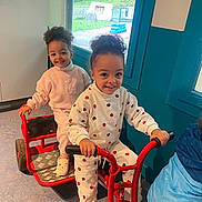 Naelle participe au concours pour gagner de l'argent avec cette photo : child, children, tricycle, indoor, red, curly_hair, smiling, play, window, greenery, sweatshirt, pants, footwear, floor, hand, toy, fun, happy, person, casual