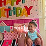 toddler, child, birthday, party, gifts, pink, banner, present, smile, happy, indoor, clothing, tank_top, shorts, hair_bun, celebration, decorations, table, wrapped_gifts, person