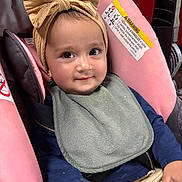 Regina joined the competition — help win amazing prizes! baby, child, infant, smiling, portrait, stroller, car_seat, bow, headband, bib, clothing, sitting, indoors, close_up, face, eyes, happy, adorable, safety_label, vehicle_seat