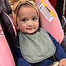 baby, child, infant, smiling, portrait, stroller, car_seat, bow, headband, bib, clothing, sitting, indoors, close_up, face, eyes, happy, adorable, safety_label, vehicle_seat