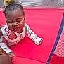 baby, child, pajamas, crawling, laughing, happy, inflatable, red_surface, indoor, play, curly_hair, smiling, tongue_out, person, infant, cute, fun, joyful, colorful_clothing, face