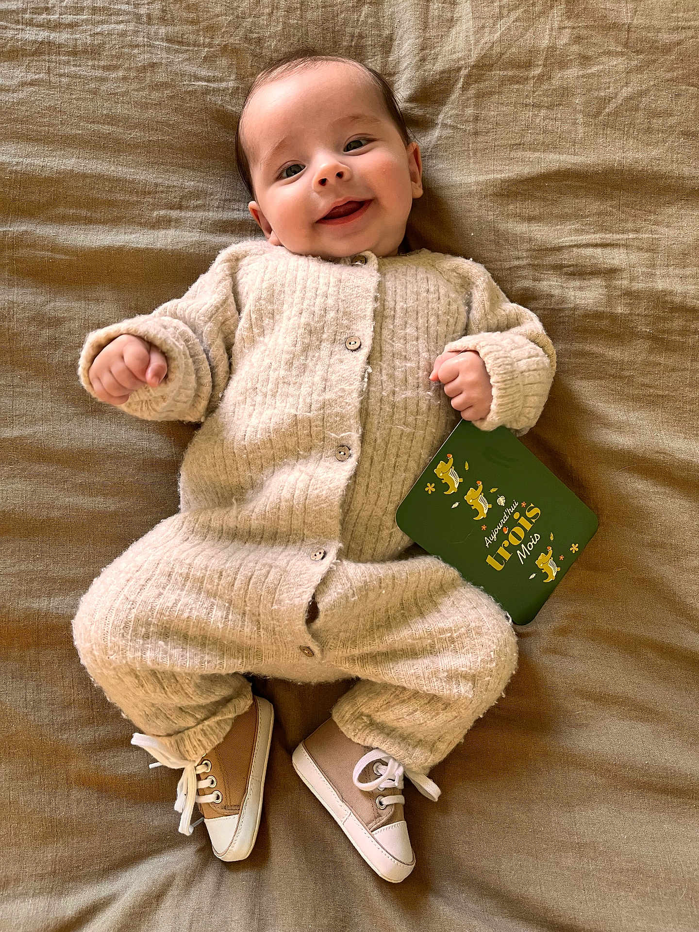 Maë a rejoint le concours — aidez-le/la à gagner de superbes lots ! baby, infant, smiling, cozy_clothing, knitwear, shoes, lying_down, blanket, card, age_marker, happy, cute, child, portrait, indoors, soft_texture, buttoned_outfit, small_hands, feet, casual