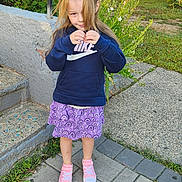 Kenzie is registered to the contest to win money with this photo: child, girl, outdoor, playground, sneakers, hoodie, skirt, pavement, stairs, plants, grass, daylight, casual_clothing, hair, person, smiling, nature, play, background, garden