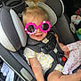 Kinsley is registered to the contest to win money with this photo: toddler, child, car_seat, sunglasses, pink, flower_shaped, beads, hair_tie, pony_tail, doll, car_interior, seat_belt, clothing, yellow, white, smiling, happy, baby, drink_cup, toy