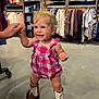 Kinsley is registered to the contest to win money with this photo: toddler, child, baby, cowboy_boots, pink_romper, clothing_store, clothes_rack, smiling, holding_hands, standing, blonde_hair, hair_tied, floor, shopping, retail, casual, indoor, person, happy, cute