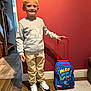 child, boy, smile, indoor, backpack, marvel, sneakers, sweatshirt, pants, wood_floor, carpet, wall, red_wall, handrail, doorway, light, shadow, person, standing, happy