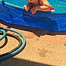 toddler, child, pool, blue_pool, water, pacifier, outdoor, sunlight, concrete, hose, garden, summer, playtime, fence, toy, curly_hair, pink_swimsuit, shadow, daytime, backyard