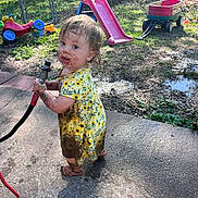 Everleigh is registered to the contest to win money with this photo: toddler, child, mud, yellow_dress, hose, outdoor, playground, slide, wagon, grass, concrete, barefoot, dirt, summer, garden, backyard, toy, messy, curious, person