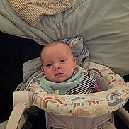 August is registered to the contest to win money with this photo: baby, infant, child, bouncer, baby_bouncer, bib, striped_shirt, blanket, bed, bedding, pillow, legs, feet, toes, face, portrait, indoors, home, patterned_fabric, cute