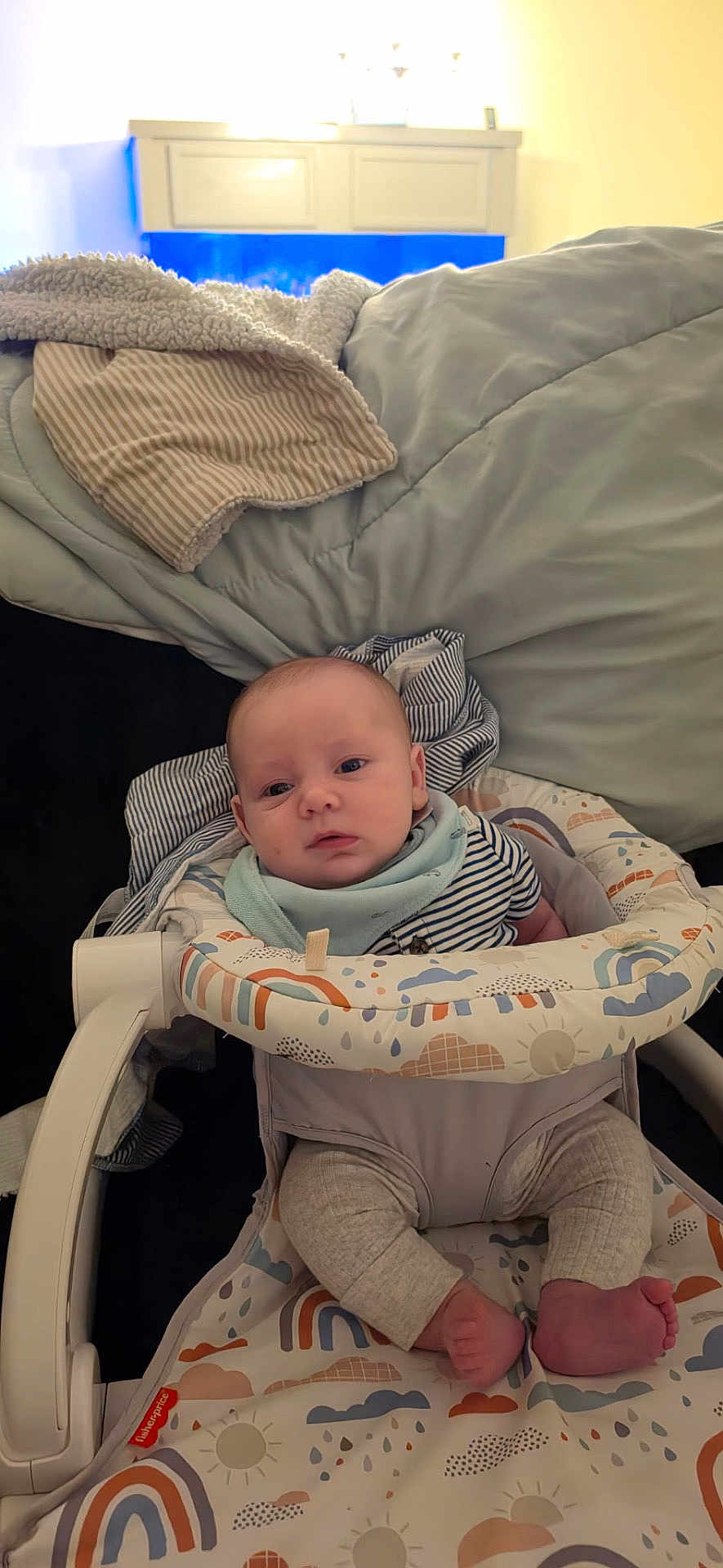 August is registered to the contest to win money with this photo: baby, infant, child, bouncer, baby_bouncer, bib, striped_shirt, blanket, bed, bedding, pillow, legs, feet, toes, face, portrait, indoors, home, patterned_fabric, cute