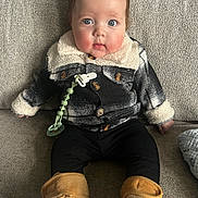 Oliver joined the competition — help win amazing prizes! baby, child, infant, plaid_jacket, black_leggings, tan_booties, pacifier_clip, couch, gray_couch, sitting, indoor, curious_look, rosy_cheeks, cozy_clothing, portrait, young_child, cute, warm_clothing, fuzzy_collar, comfortable