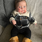 Louie is registered to the contest to win money with this photo: baby, child, infant, smiling, plaid_jacket, boots, black_leggings, couch, blanket, cozy, indoor, cute, child_wearing_clothes, furniture, portrait, chubby_cheeks, warm_clothing, relaxed, seated, happy