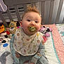 baby, pacifier, crib, toy, quilt, baby_clothing, bib, indoor, child, bed, cute, infant, face, hair, playroom, smile, person, colorful, plush_toy, sleepwear