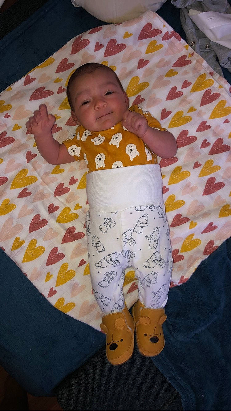 Keïla participe au concours pour gagner de l'argent avec cette photo : arm, baby, baby_toddler_clothing, barefoot, bed_sheet, bedding, child, comfort, face, human_leg, knee, linens, pajamas, pattern, person, sleeve, smile, t_shirt, textile, thigh