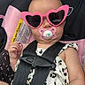 baby, child, pacifier, sunglasses, heart_shaped, car_seat, safety_harness, pink, cute, infant, clothing, black_straps, white_outfit, patterned, face, portrait, seat, restraint, accessory, young