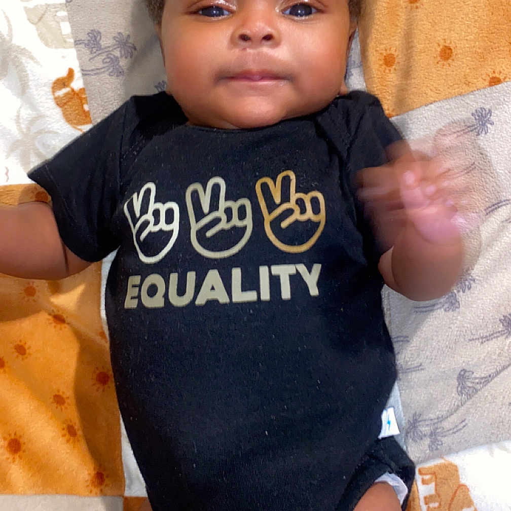 Trelyn joined the competition — help win amazing prizes! arms, baby, black_clothing, blanket, child, closeup, cute, equality, hand_gesture, human, indoors, infant, legs, lying_down, onesie, patterned_blanket, peace_sign, skin, smiling_face, soft_lighting