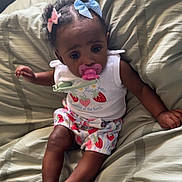 Kinsley joined the competition — help win amazing prizes! baby, child, pacifier, hair_bow, bed, blanket, clothing, sandals, infant, cute, curly_hair, person, indoors, portrait, sitting, strawberry_print, small_shoes, toddler, young_child, comfortable