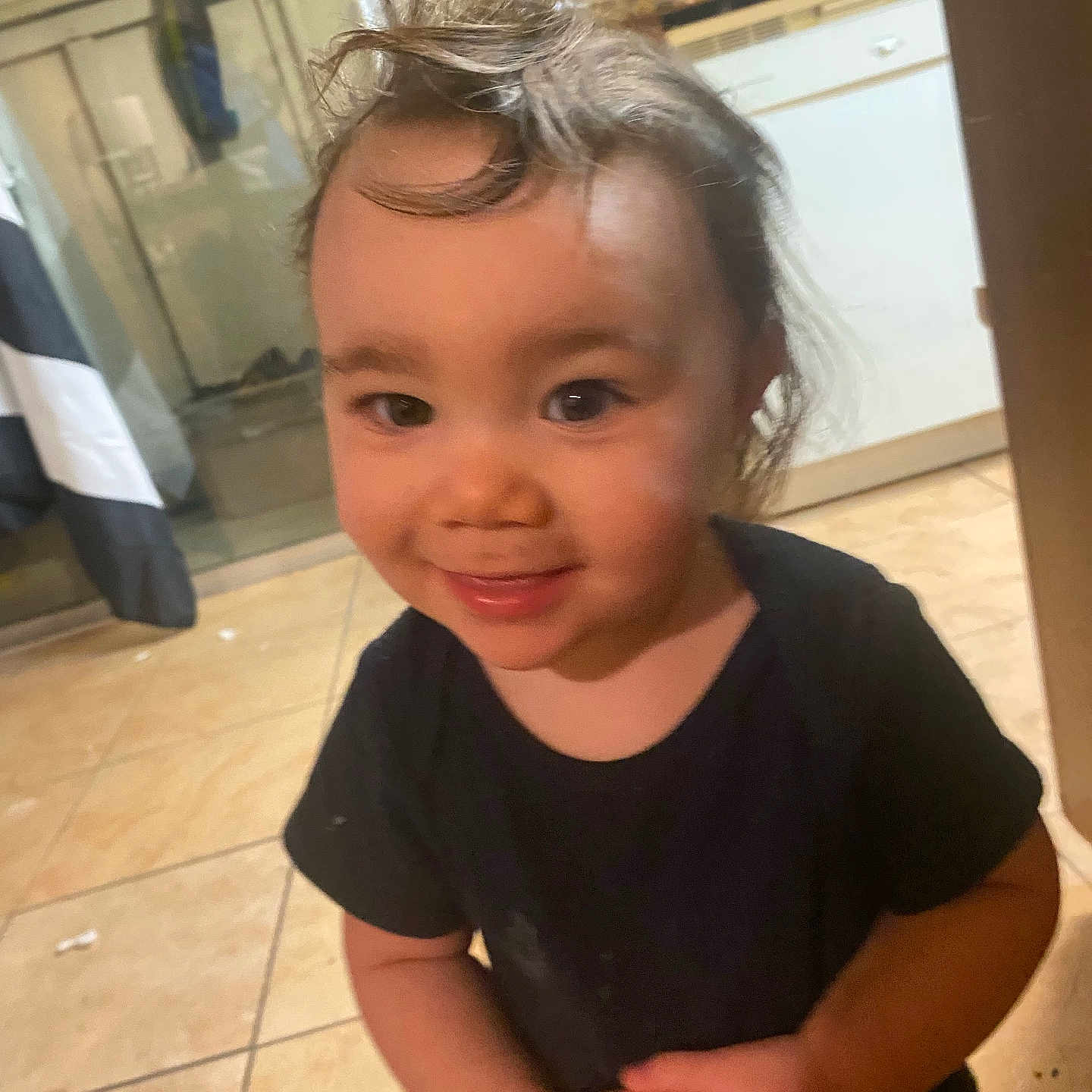 Zaylee is registered to the contest to win money with this photo: black_shirt, cabinet, child, cute, domestic, face, hair, happy, home, indoor, kitchen, messy_hair, natural_light, person, playful, smiling, standing, tile_floor, toddler, young_child