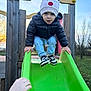 Mayron participe au concours pour gagner de l'argent avec cette photo : child, toddler, slide, playground, hat, beanie, puffer_jacket, sneakers, hand, adult_hand, wooden_structure, grass, trees, sky, sunset, outdoor, park, playtime, portrait, candid