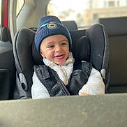 Mayron participe au concours pour gagner de l'argent avec cette photo : child, baby, infant, car_seat, seatbelt, beanie, hat, smile, happy, teeth, jacket, fleece, winter_clothing, rear_seat, car_interior, window, blurred_background, cozy, portrait, candid