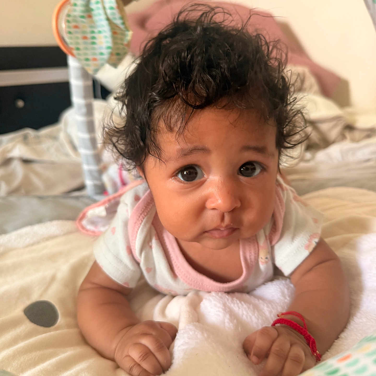Ahzyna is registered to the contest to win money with this photo: baby, infant, curly_hair, blanket, bed, soft_toys, indoor, cute, portrait, child, young, person, pink_clothing, expression, face, hands, lying_down, closeup, cozy, warm