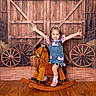 Dreamiee is registered to the contest to win money with this photo: child, girl, smiling, rocking_horse, wooden_floor, barn_backdrop, denim_dress, pink_bows, cowboy_boots, happy, arms_outstretched, playful, indoor, portrait, toy, wooden_wheels, rustic, flooring, cute, posing