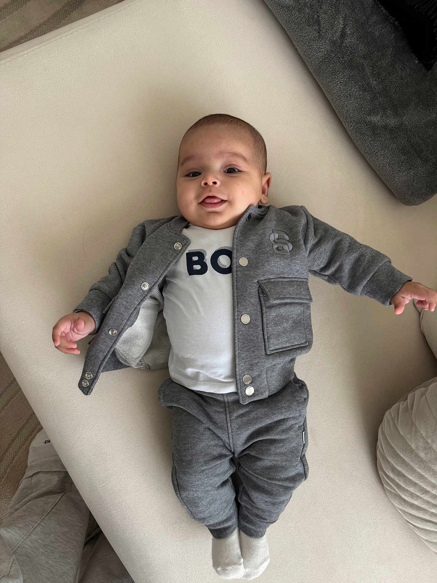 Isaac participe au concours pour gagner de l'argent avec cette photo : baby, blanket, child, couch, cozy, cute, face, grey_clothing, indoor, infant, jacket, lying_down, pants, person, playful, smile, socks, soft_surface, tongue, young_child
