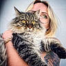 cat, tabby_cat, fluffy, long_hair, pet, animal, yellow_eyes, whiskers, portrait, woman, glasses, blonde_hair, human, holding_pet, tattoo, arm, close_up, indoor, cute, photography