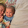 baby, child, smile, bed, blanket, patterned_blanket, pillow, indoor, happy, face, person, cute, sibling, family, cozy, head, lying_down, comfort, young_child, expression