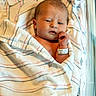 newborn, baby, infant, child, face, portrait, lying_down, blanket, hospital, wristband, sleeping, awake, wide_eyes, hand, skin, striped_fabric, indoor, photograph, maternity, birth