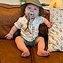 baby, child, pacifier, hat, bucket_hat, shirt, shorts, couch, pillow, indoor, furniture, portrait, sitting, cute, infant, hand, foot, face, expression, home