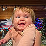 american_flag, baby, background, blue_eyes, cheeks, child, cute, face, festive_lights, hand, happy, holding, holiday, indoor, joyful, person, pink_sweater, portrait, smiling, warm_lighting