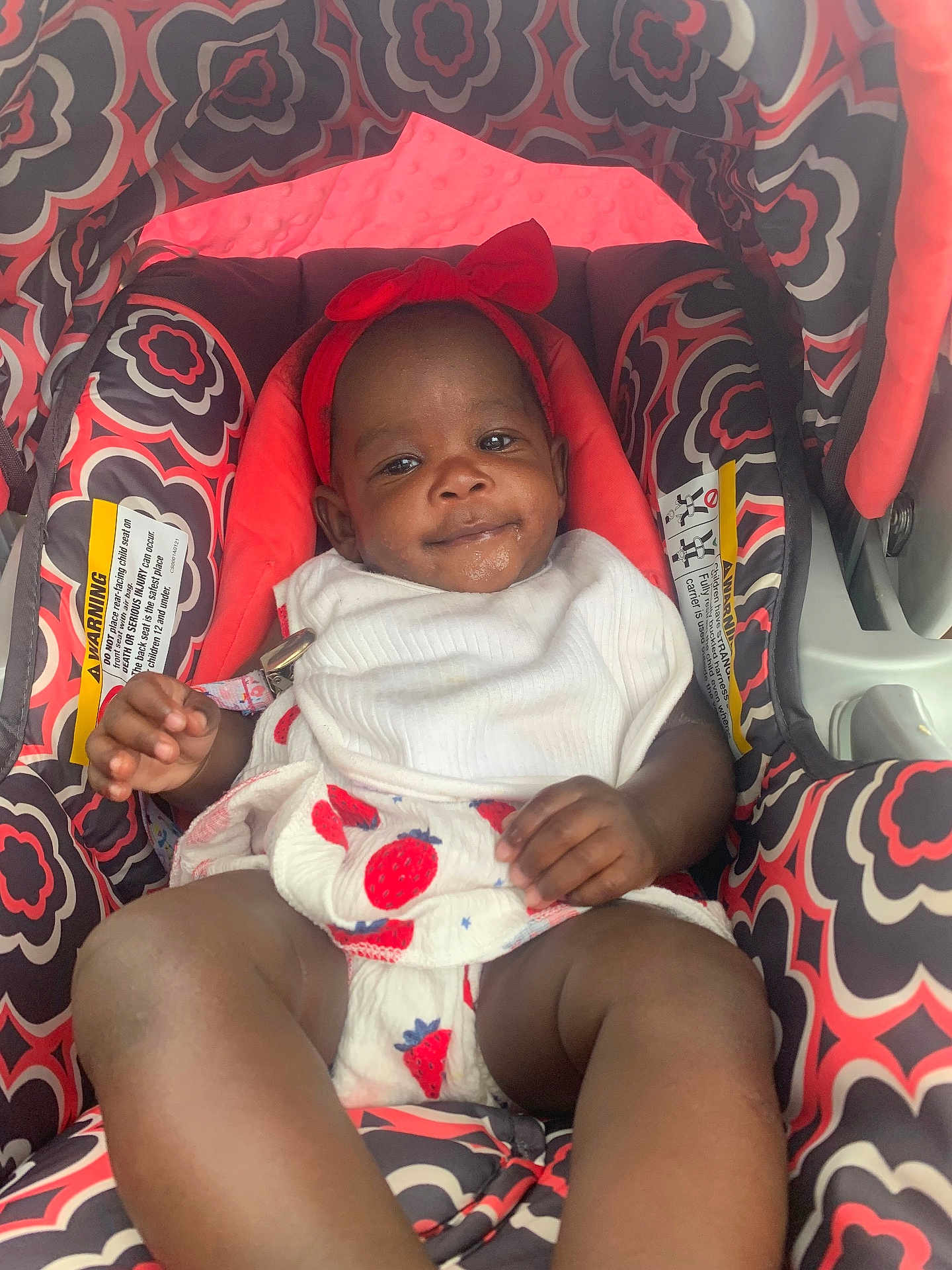 Dajana Miles is registered to the contest to win money with this photo: baby, infant, car_seat, headband, red_bow, patterned_fabric, strawberry_print, white_clothing, drool, smile, child, cute, seat, comfort, indoor, person, young_child, relaxing, portrait, baby_clothes