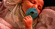 Oakleigh is registered to the contest to win money with this photo: baby, blanket, blue, child, clothing, cozy, cute, face, hand, indoors, infant, newborn, pacifier, patterned_background, peaceful, pink, portrait, resting, sleeping, soft_texture