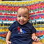 baby, child, smiling, face, person, clothing, toddler, indoor, patterned_fabric, colorful, seat, cute, happy, portrait, apparel, sitting, one_piece, young_child, infant, casual