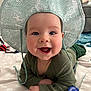 baby, child, smiling, hat, green_clothing, lying_down, indoor, face, happy, closeup, cute, infant, person, apparel, pattern, fabric, hand, blue_tag, soft_surface, cheerful