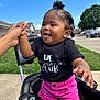 beads, black_shirt, blue_sky, braided_hair, child, cute, daylight, grass, hand_holding, happy, outdoor, person, playful, residential_area, shorts, sidewalk, smiling, stroller, summer, toddler