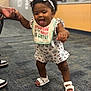 adult_hand, baby, carpet, child, clothing, cute, floor, footwear, hand_holding, happy, headband, indoor, infant, person, romper, smiling, support, toddler, tongue_out, walking