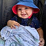 Noah is registered to the contest to win money with this photo: baby, smiling, blue_hat, red_hat, blanket, animal_print, stroller, child, happy, cute, infant, clothing, outdoor, sunlight, portrait, hand, face, seat_belt, fabric, comfort