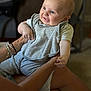 baby, child, smiling, indoor, person, adult_hands, bib, clothing, gray_pants, blue_eyes, short_hair, holding, sitting, happy, infant, cute, human, portrait, skin, arm