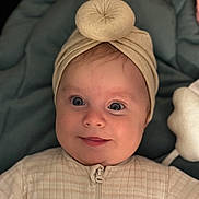 Denise participe au concours pour gagner de l'argent avec cette photo : baby, infant, smile, face, headwear, turban, clothing, onesie, blue_cushion, plush_toy, indoor, portrait, cute, child, young, closeup, happy, soft_lighting, baby_girl, cozy