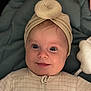 baby, infant, smile, face, headwear, turban, clothing, onesie, blue_cushion, plush_toy, indoor, portrait, cute, child, young, closeup, happy, soft_lighting, baby_girl, cozy