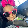 toddler, child, sunglasses, pink_bow, car_seat, seatbelt, smile, curly_hair, casual_clothing, portrait, indoor, cute, fashion, baby, headwear, accessory, seat, car_interior, sunlight, closeup
