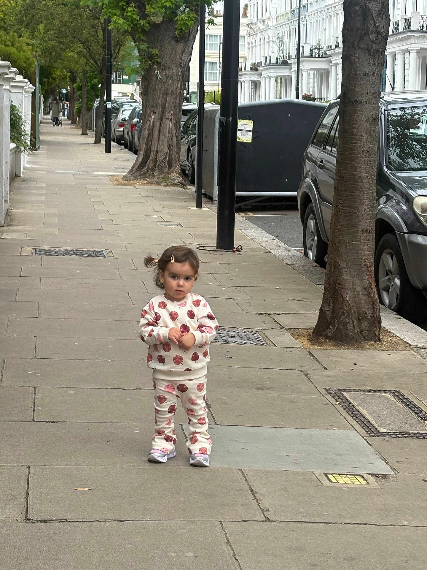 Arianna joined the competition — help win amazing prizes! toddler, child, sidewalk, street, trees, cars, urban, buildings, clothing, footwear, person, hairclip, pavement, daytime, outdoor, curious, standing, matching_outfit, casual, city
