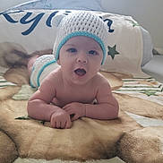 Kylian a rejoint le concours — aidez-le/la à gagner de superbes lots ! baby, infant, tummy_time, crocheted_hat, open_mouth, cute, blanket, bed, pillow, curtain, window_light, diaper, hands, skin, portrait, smile, cozy, soft_texture, looking_at_camera, nursery