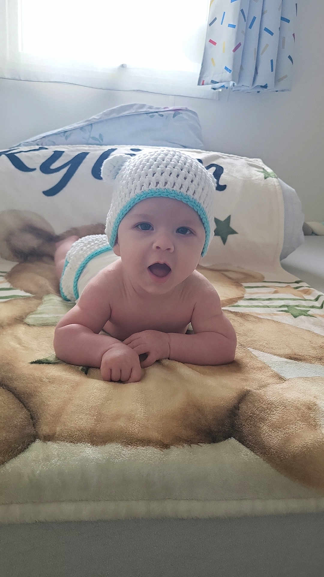 Kylian a rejoint le concours — aidez-le/la à gagner de superbes lots ! baby, infant, tummy_time, crocheted_hat, open_mouth, cute, blanket, bed, pillow, curtain, window_light, diaper, hands, skin, portrait, smile, cozy, soft_texture, looking_at_camera, nursery