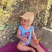 Lúccia participe au concours pour gagner de l'argent avec cette photo : barefoot, casual, cheeky, cheese_puffs, child, cute, happy, hat, outdoor, playful, purple_towel, sitting, smiling, snack, stone_wall, summer, sunlight, swimsuit, toddler, young_child