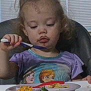 Echo joined the competition — help win amazing prizes! toddler, child, high_chair, spoon, plate, food, curly_hair, purple_shirt, frozen_characters, indoor, eating, meal, window_blinds, table, concentration, young_child, person, dining, seat, messy_face