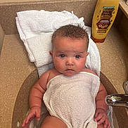 Harper is registered to the contest to win money with this photo: baby, towel, sink, bathroom, child, water, curly_hair, blue_eyes, skin, faucet, countertop, bottle, conditioner, clean, cute, infant, person, sitting, wrapped, plump