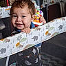 Lucius is registered to the contest to win money with this photo: baby, child, toddler, curly_hair, smiling, happy, face, portrait, indoor, playpen, crib, nursery, toy, musical_toy, animal_pattern, elephant, giraffe, colorful, sitting, playtime
